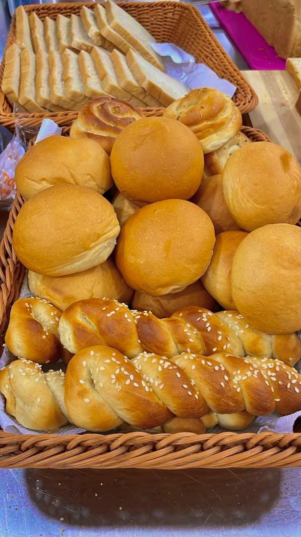 Una cesta llena de diferentes tipos de pan, incluyendo bollos redondos y panes trenzados.