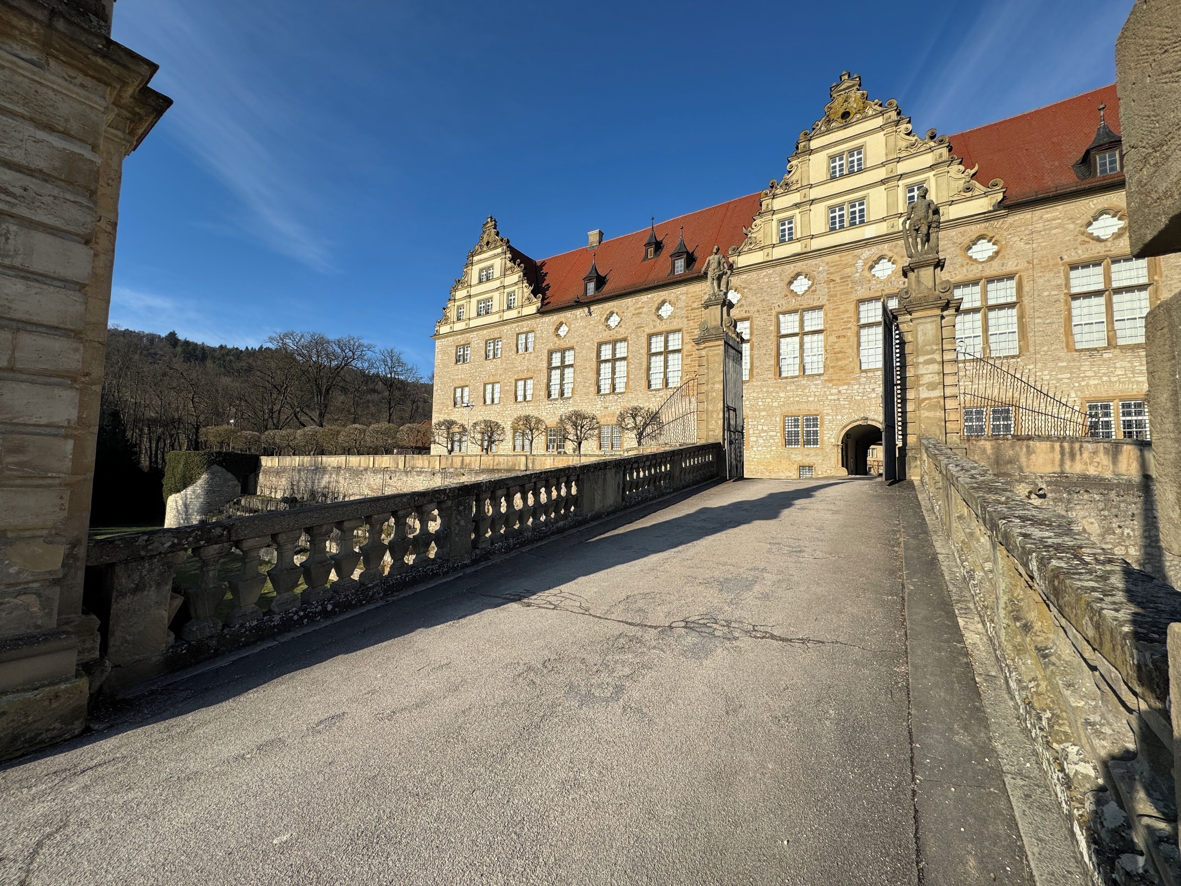 Un bâtiment historique avec un toit rouge, de grandes fenêtres et un pont de pierre à l’avant.