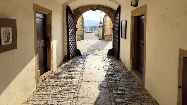 A cobblestone pathway leading to a gate, flanked by arched doorways and framed pictures on the walls. - Green oasis in Weikersheim, close to the center in a very quiet location. (Weikersheim)