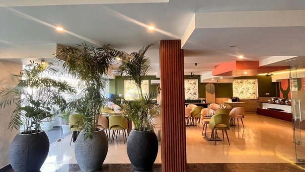 A modern lobby with marble flooring, large potted plants, and a seating area with yellow chairs. - PINK GUAVA HOTELS (Gurugram)