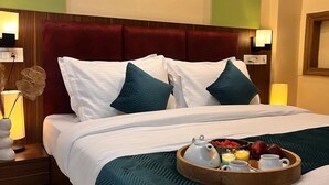 A hotel room with a large bed, a wooden headboard, and a tray of breakfast items on the bed. - PINK GUAVA HOTELS (Gurugram)