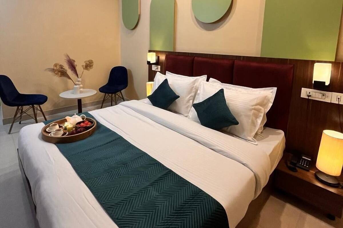 A hotel room with a bed, bedside table, lamp, and a small table with chairs.