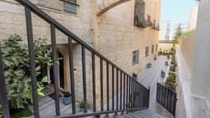 Un bâtiment en pierre doté d’un escalier et d’une balustrade, de plantes en pot, et d’où l’on peut apercevoir un autre bâtiment au loin.