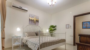 Une chambre à coucher comprenant un lit, une table de chevet, une lampe, un appareil de climatisation et un tableau accroché au mur.