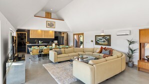 Een ruime woonkamer met een grote beige hoekbank, een glazen salontafel, en een eetgedeelte met een houten tafel en stoelen.