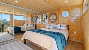Een moderne slaapkamer met houten wanden, een groot bed met kussens en beddengoed in teal- en witte tinten, en een grote spiegel die de kamer weerspiegelt.