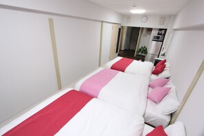 Une chambre d’hôtel avec deux lits, chacun doté de draps blancs et rouges, une petite kitchenette et un miroir au mur.