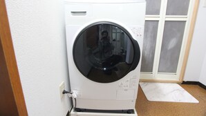 A front-loading washing machine in a room with a white door and a small white mat on the floor. - Shinjuku Kabukicho* 2DK / MAX 10 people / FREE WiFi (新宿区大久保)