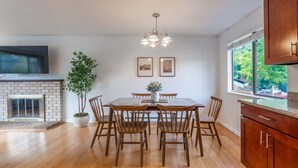 Un comedor con una mesa y sillas de madera, una chimenea, un ventanal grande y una zona de cocina con armarios de madera.