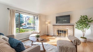 Una sala de estar moderna con chimenea, un ventanal con cortinas, un televisor de pantalla plana y una planta en maceta.