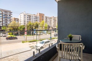 Private balcony with two chairs, a round table, and a leafy city outlook—an inviting spot to enjoy morning coffee above the avenue. - Modern Studio in Las Condes with Gym & BBQ (Las Condes)