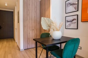 Private dining area with two emerald-green chairs, a dark table, wood cabinetry, and curated abstract artwork. - Modern Studio in Las Condes with Gym & BBQ (Las Condes)