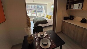 Une chambre d’hôtel moderne avec balcon, un coin repas avec une table dressée pour deux personnes et une kitchenette.