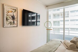 Hotellihuone, jossa on sänky, kehystetty taulu, litteänäyttöinen televisio ja ikkuna, josta on näkymä rakennuksiin.