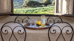 A dining table with a tray holding glasses, lemons, and a pitcher, set against a scenic view of a green landscape through a window.