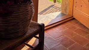 A wicker basket with flowers on a chair, a wooden door leading to an outdoor area with a view of a hilly landscape.