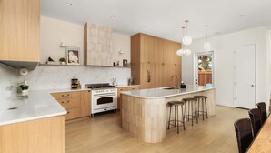 Una cucina moderna con mobili in legno, un'isola centrale con sgabelli, forno integrato e una schiena di marmo.