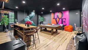 Una habitación moderna con mesa de billar, zona de bar y un gran mural con la palabra 'LOVE'.