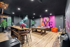 Quarto moderno com mesa de bilhar, área de bar e um grande mural com a palavra 'LOVE'.