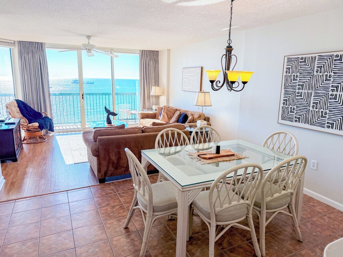A spacious living area with a glass dining table, wicker chairs, a sofa, and a view of the sea.