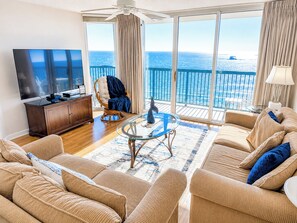 A living room with a large window, a ceiling fan, a television, and a wicker chair.