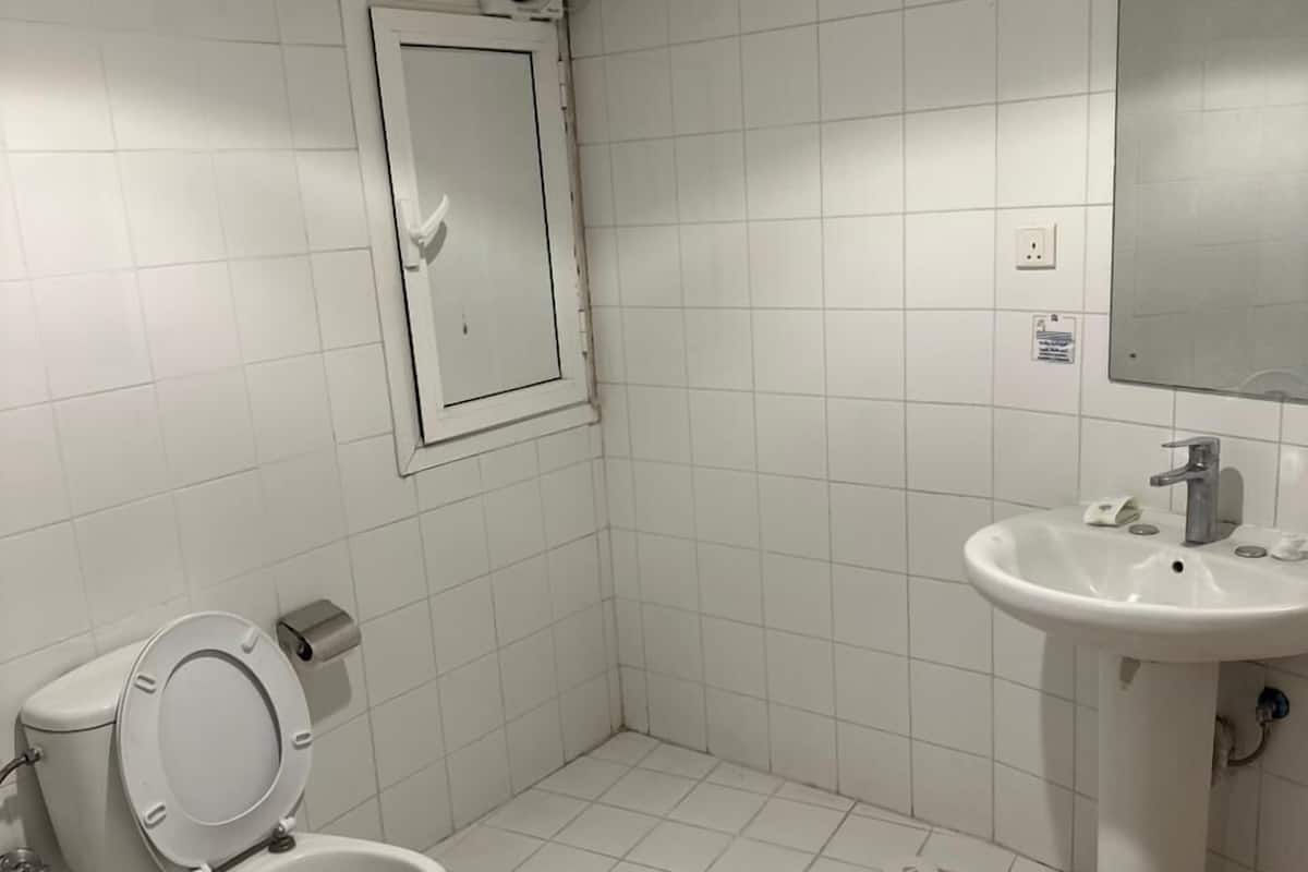A small, clean bathroom with white tiles, a toilet, a sink, and a mirror.