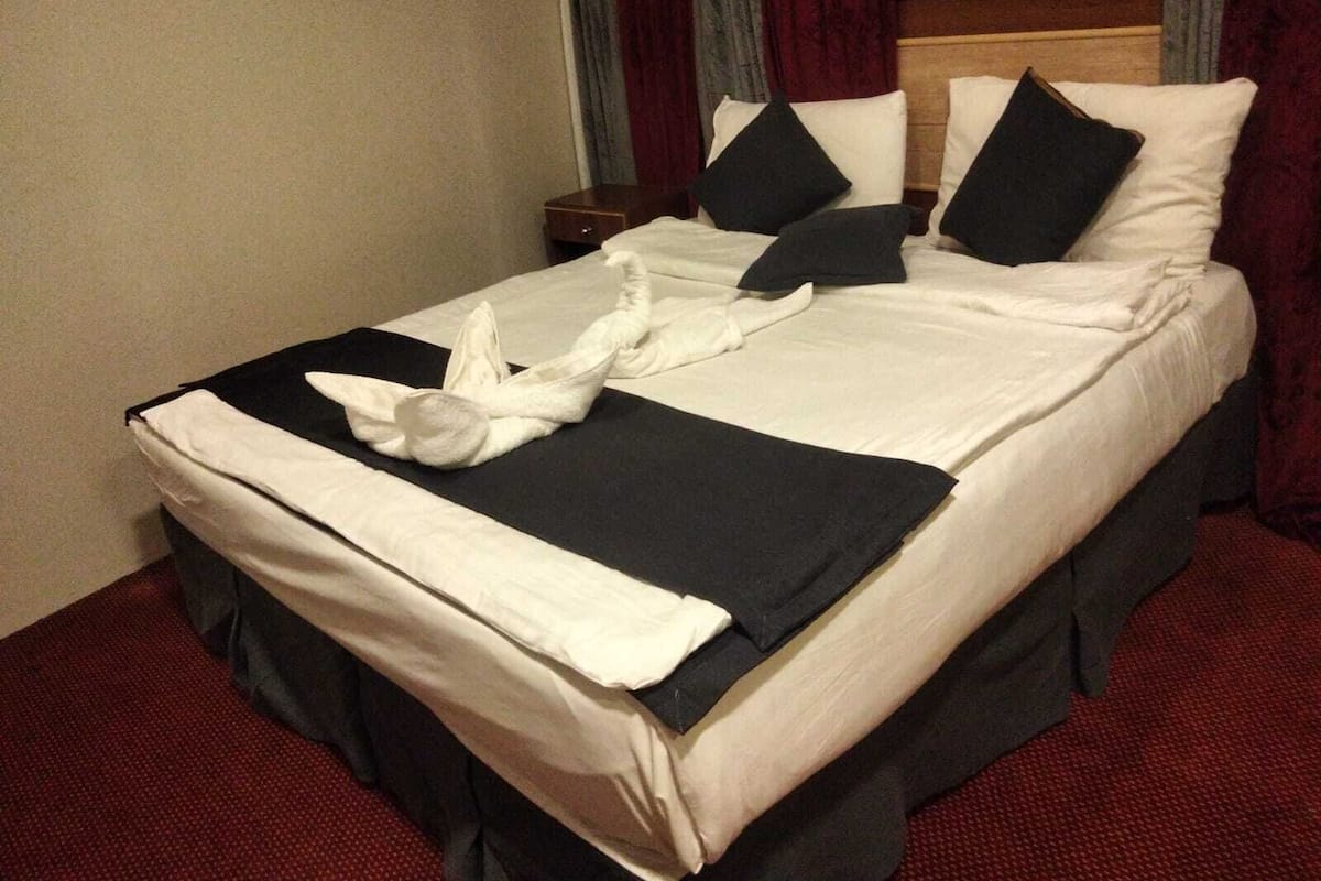 A neatly made bed with a white and black bedspread, two black pillows, and a white towel folded in the center.