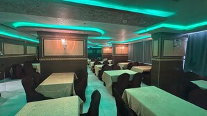 Ein Restaurant mit Tischen, die mit weißen Tischdecken gedeckt sind, mit dunklen Stühlen in einer Reihe angeordnet.