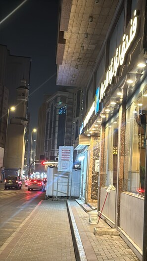 A nighttime street view with a building featuring illuminated signage and a visible entrance. - ALJEMEZA TOWER HOTEL (Makkah)