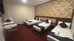 Ein Hotelzimmer mit drei Betten, einem Holzkopfende, einem roten Teppich und einem Wandpapier mit Muster.