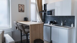 Una cocina moderna equipada con microondas, cafetera y un refrigerador pequeño. Cuenta con una mesa de comedor con sillas y un ventanal con cortinas.