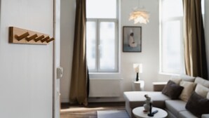Una sala de estar moderna con un sofá, una mesa de centro, una lámpara colgante y una ventana con cortinas.