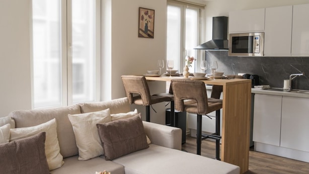 Ein modernes Wohnzimmer mit einer Couch, Sesseln, einem Esstisch und einer Küchenzeile inklusive Mikrowelle.
