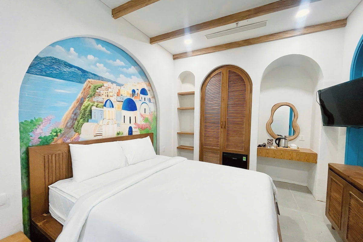 A bedroom with a bed, a wooden wardrobe, a shelf with a mirror, and a wall-mounted television.
