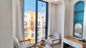 A modern room with a large window, a wooden desk with a mirror, two armchairs, and a small round table with a kettle and cups. - Pito Hotel - Hon Thom Phu Quoc (Phu Quoc)