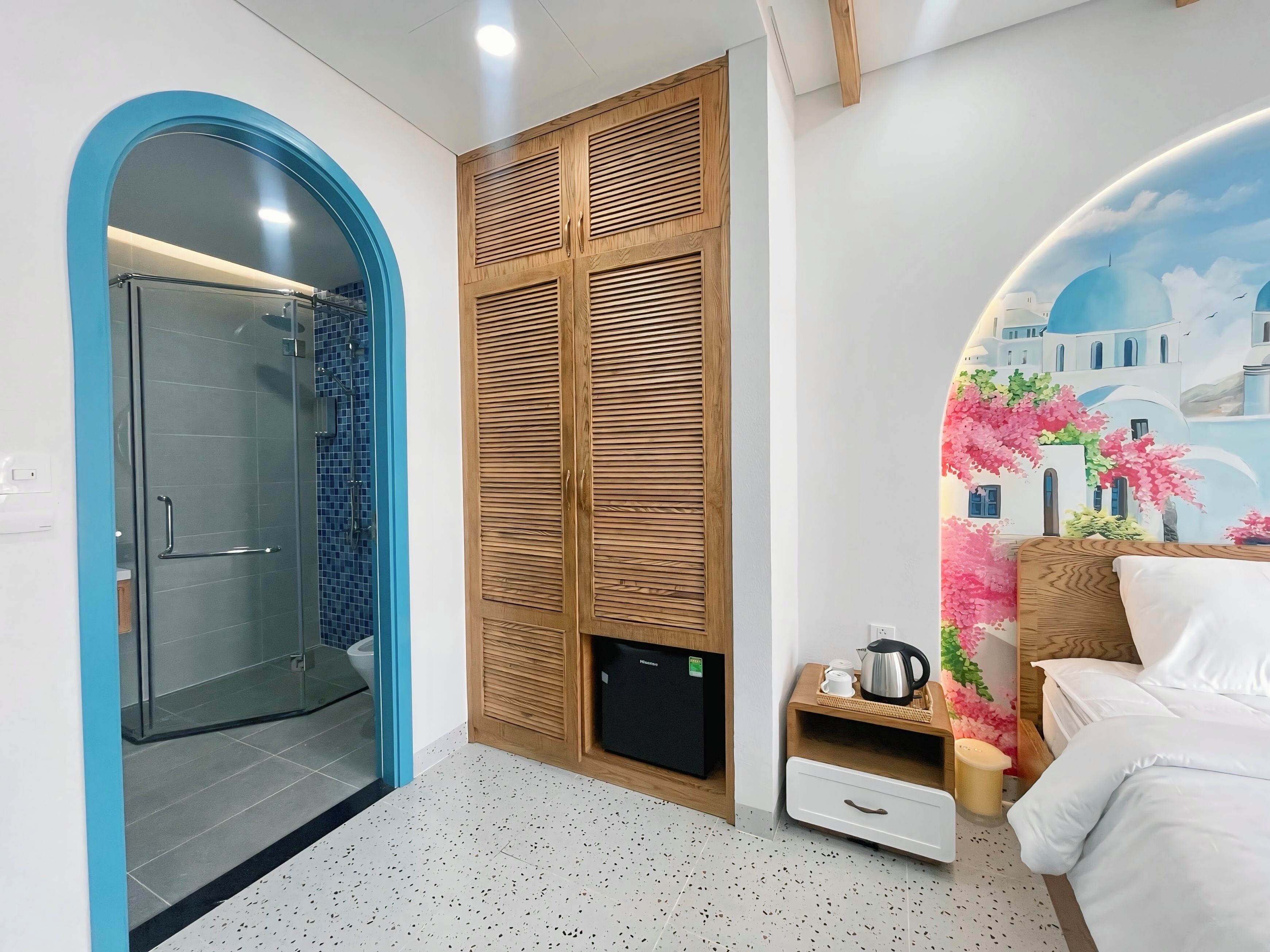 A modern bathroom with a glass shower enclosure, a wooden wardrobe, and a bed with a nightstand.
