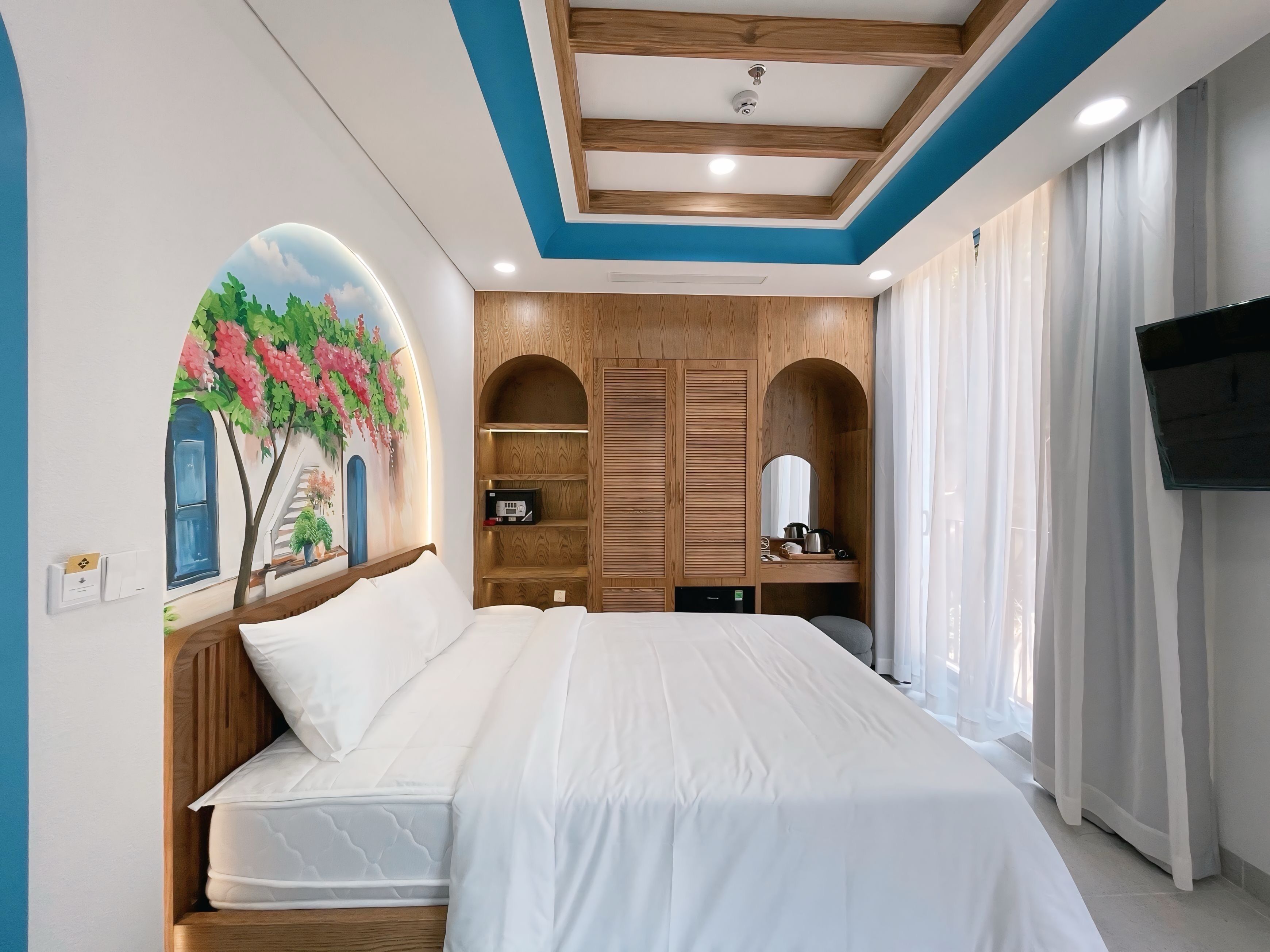 A bedroom with a bed, wooden wardrobe, built-in shelves, a TV, and a mural on the wall.