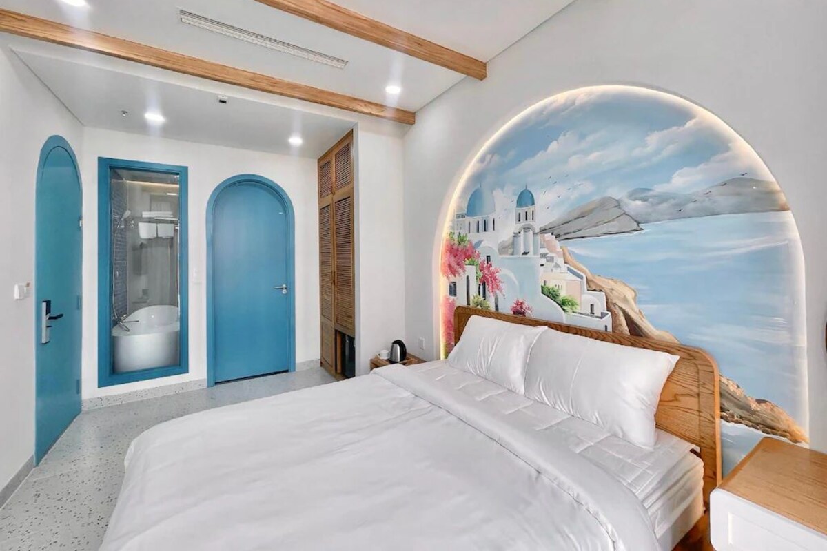 Un dormitorio con cama, ducha y un mural con una escena costera.