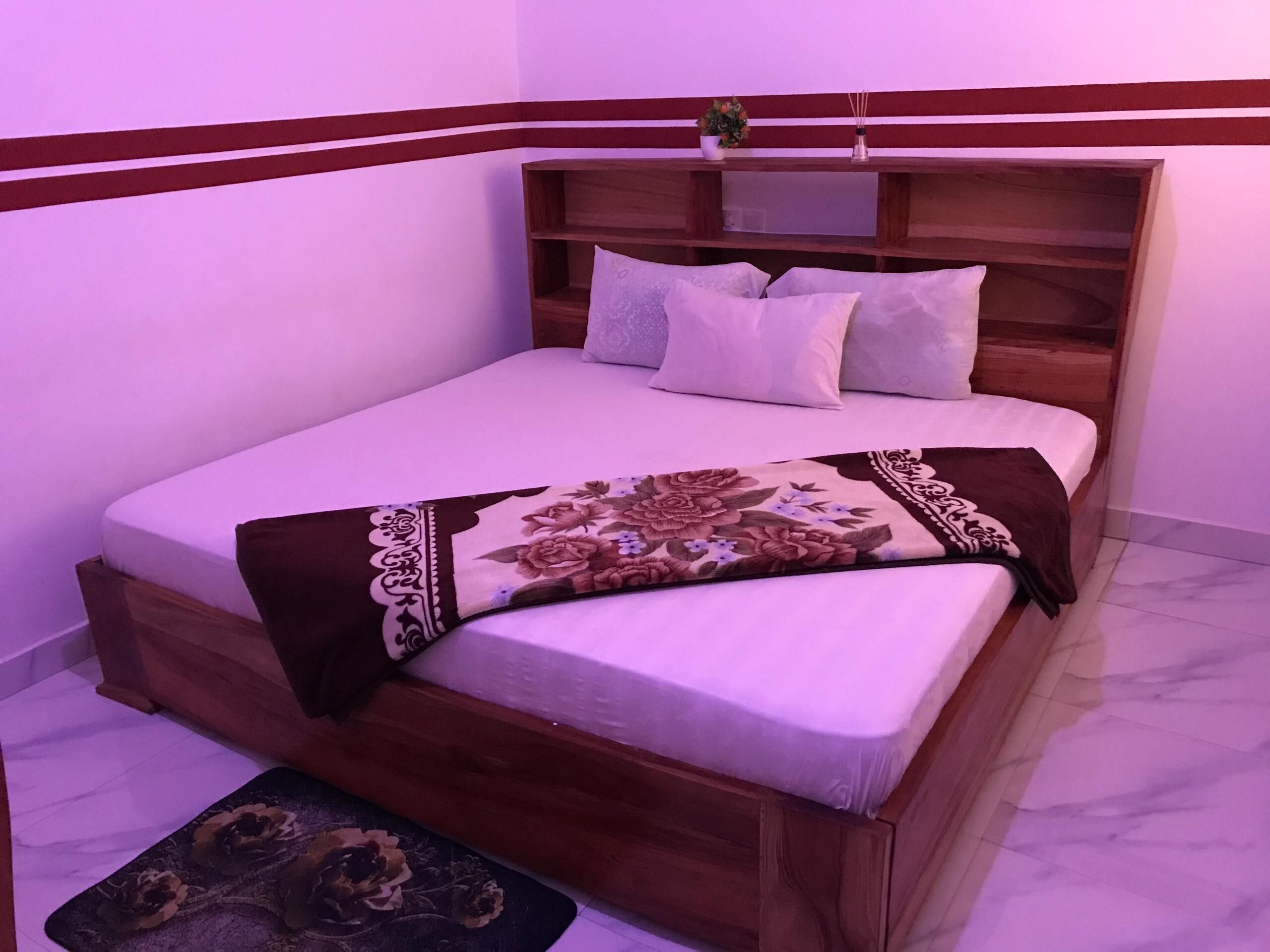 A neatly made bed with a floral bedspread, a wooden headboard, and a small bedside table with a plant.