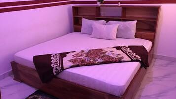 A neatly made bed with a floral bedspread, a wooden headboard, and a small bedside table with a plant.