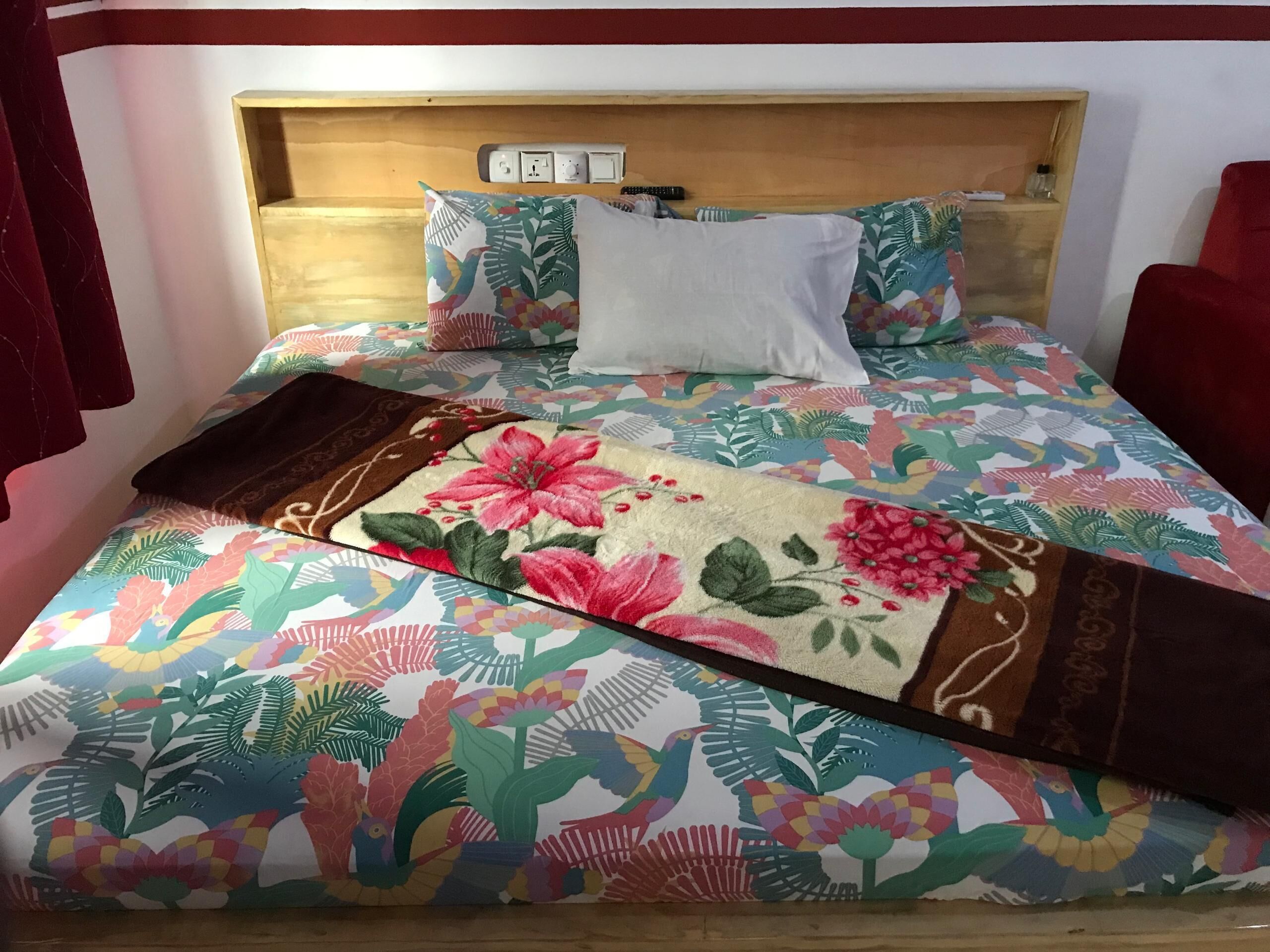 Un lit avec une couvre-lit à motifs floraux, une tête de lit en bois et un oreiller blanc.