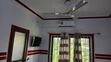 A room with a ceiling fan, an air conditioning unit, a window with curtains, and a television mounted on the wall.