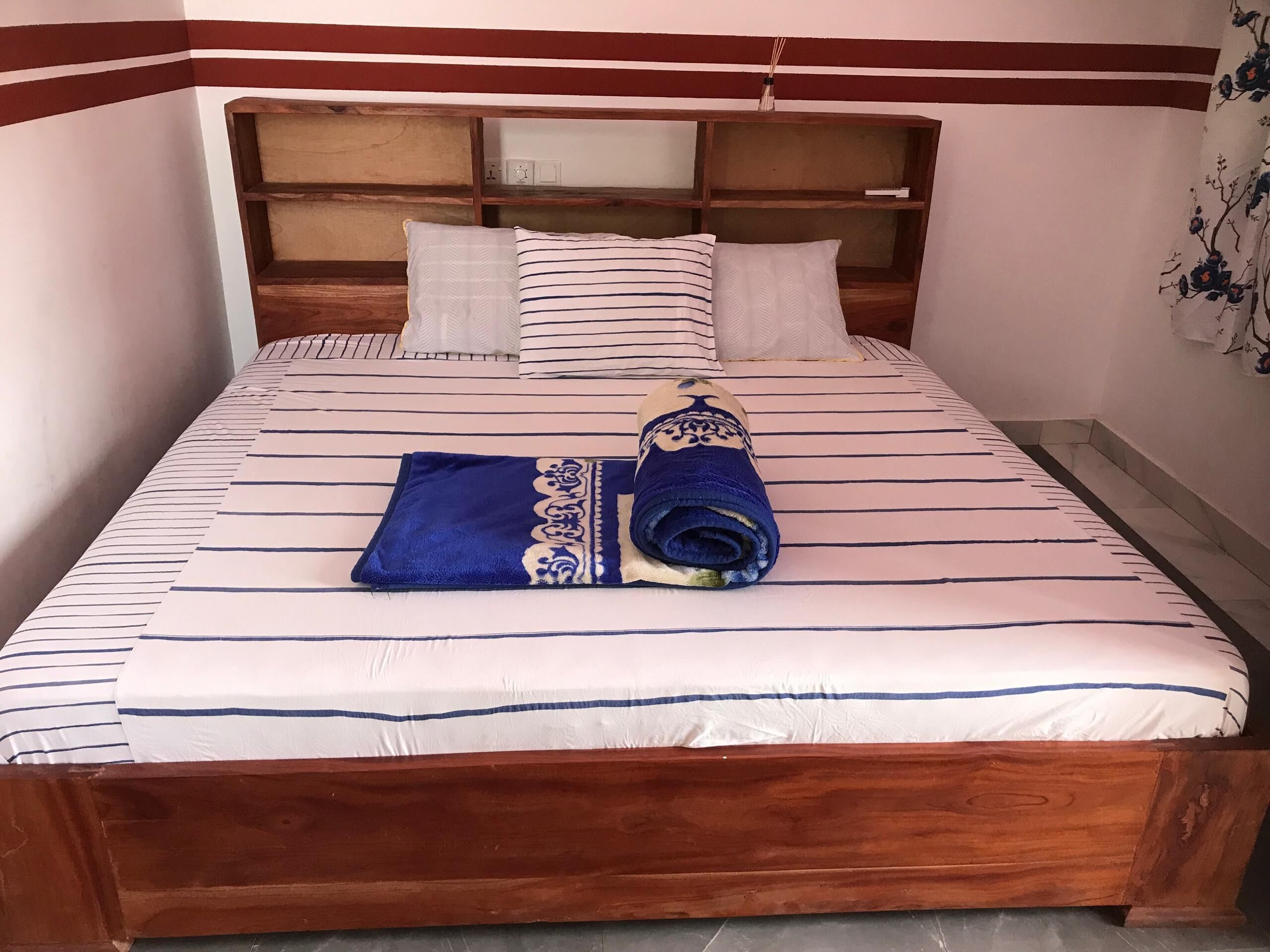 Una cama bien hecha con ropa de cama a rayas, un cabecero de madera y una toalla enrollada con un estampado azul y dorado.