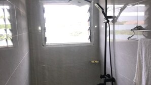 Een kleine betegelde badkamer met een douche, een raam en een handdoekhouder.