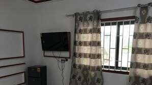 Een kamer met een flatscreen televisie aan de wand, een klein kastje en een raam met behang gordijnen.