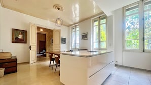 Een moderne keuken met een centraal eiland, grote ramen en een eetgedeelte.