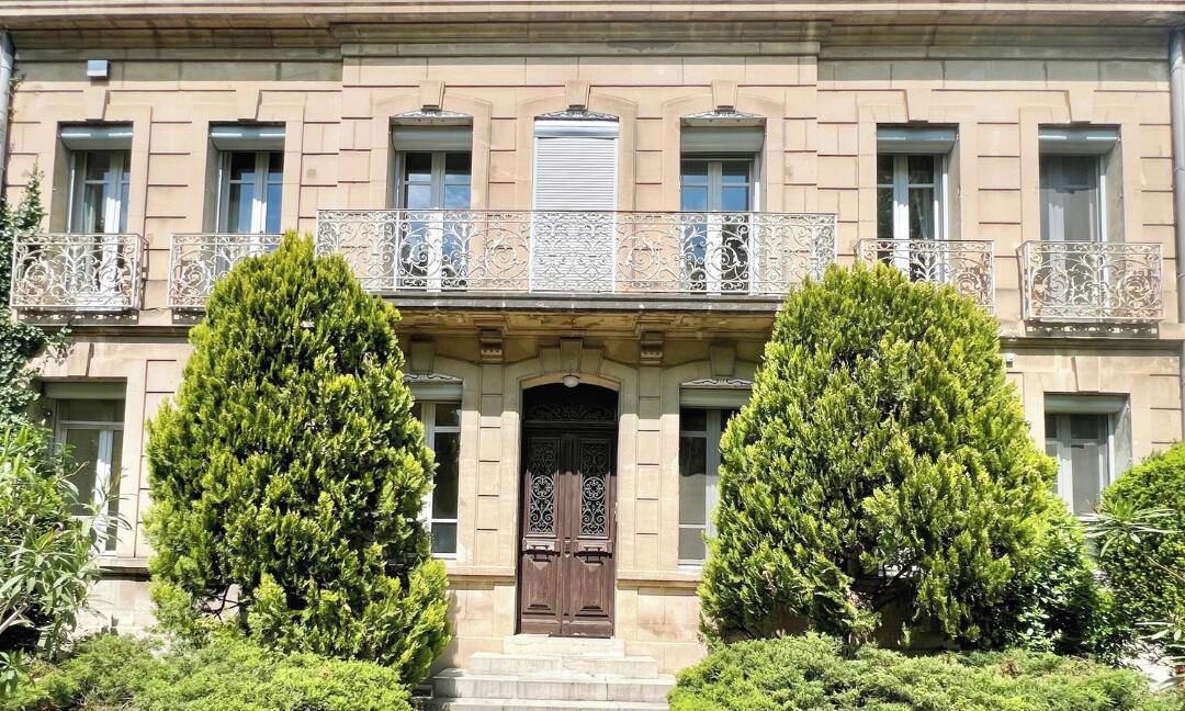 Un edificio con fachada simétrica, una entrada central con puerta decorativa y balcones ornamentados con barandillas de metal.