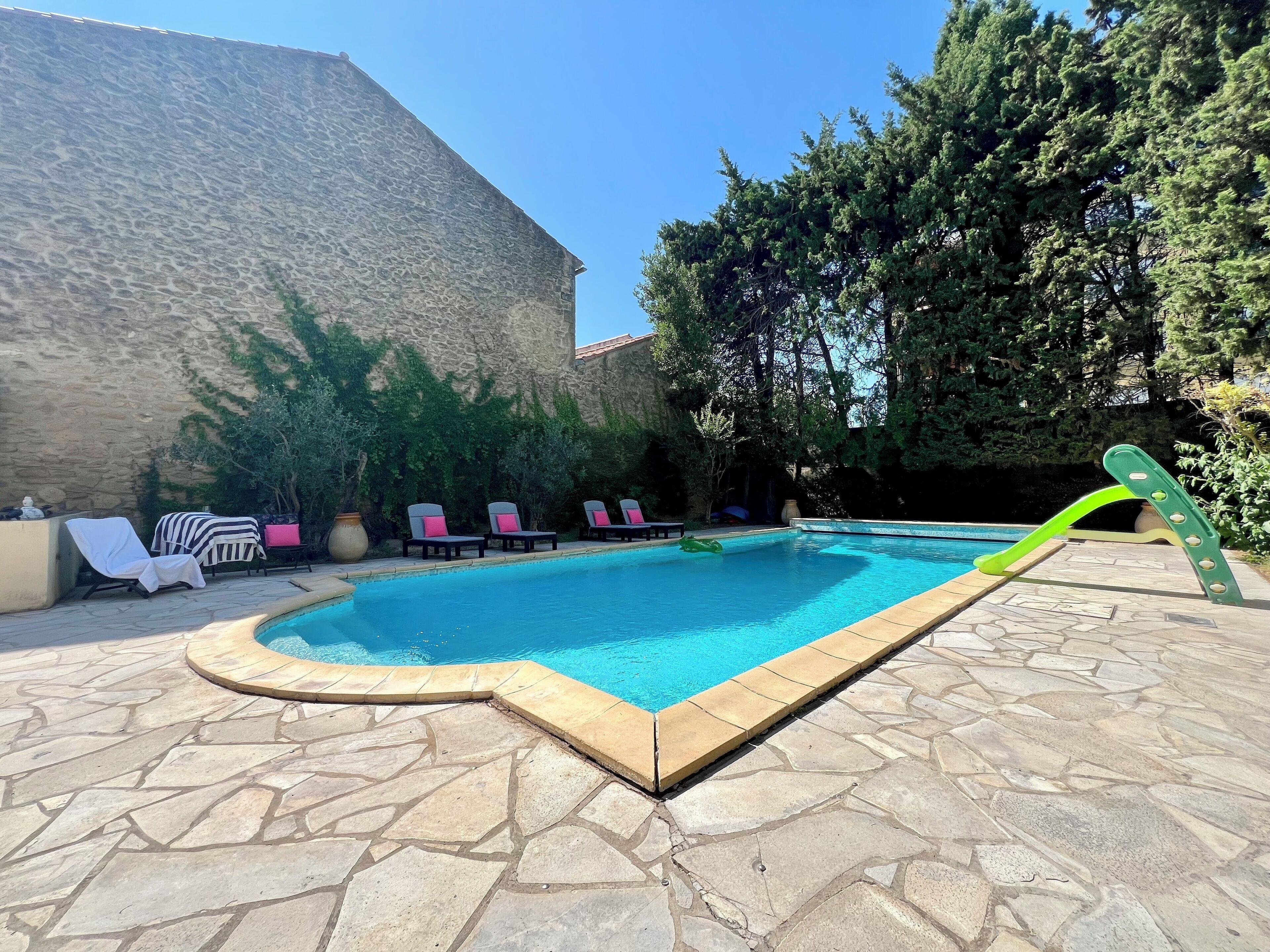 A swimming pool with lounge chairs and a stone wall in the background.