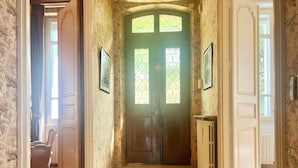 Een gang met een houten vloer, een groene deur met decoratieve glaspanelen en behang met een patroon.