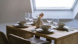 Een eettafel gedekt voor vier personen, met witte borden, kommen en wijnglazen.